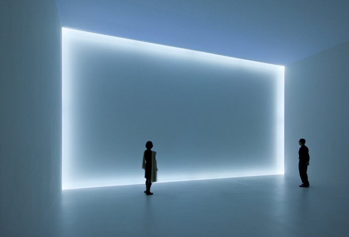 Two viewers stand in empty space, mesmerized by an empty wall that is framed by light.