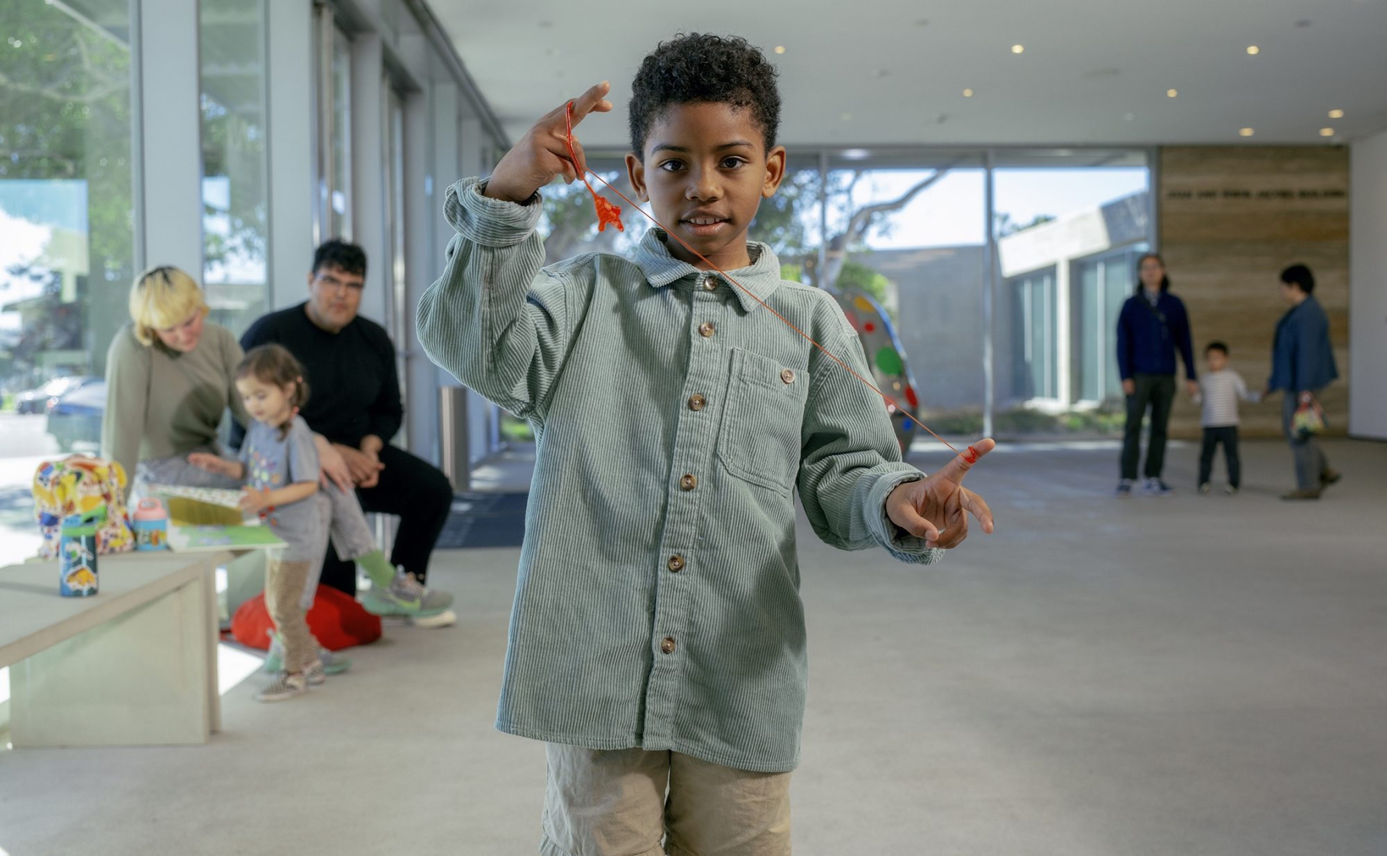 A child in the foreground playing with a bright orange toy, a family of three with a young child in the middleground and background