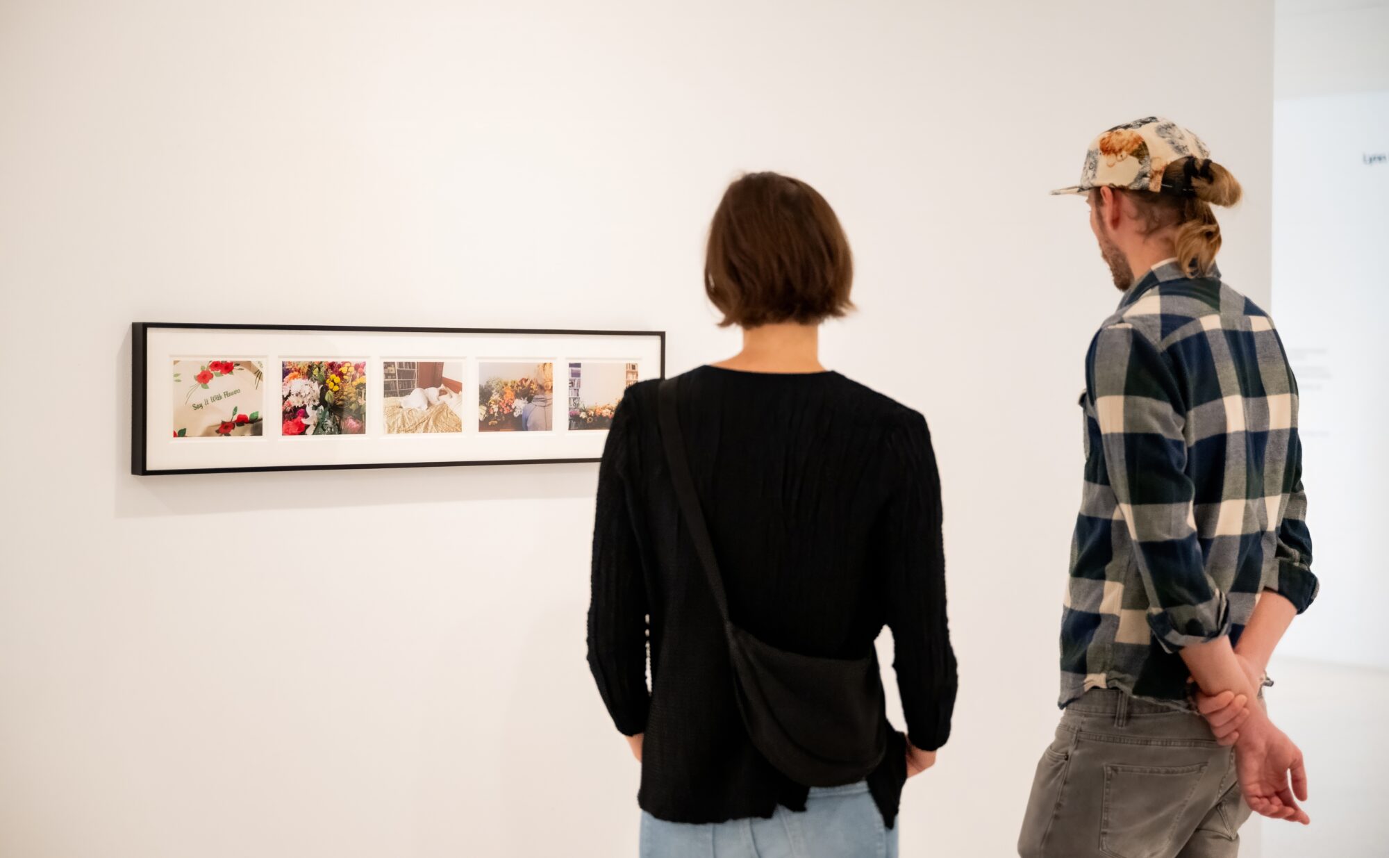 Two people look at an artwork of photographs.