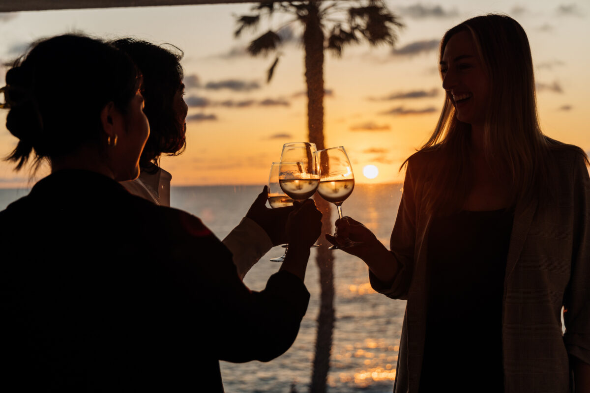 Three people toasting with wine glasses with a sunset as a backdrop