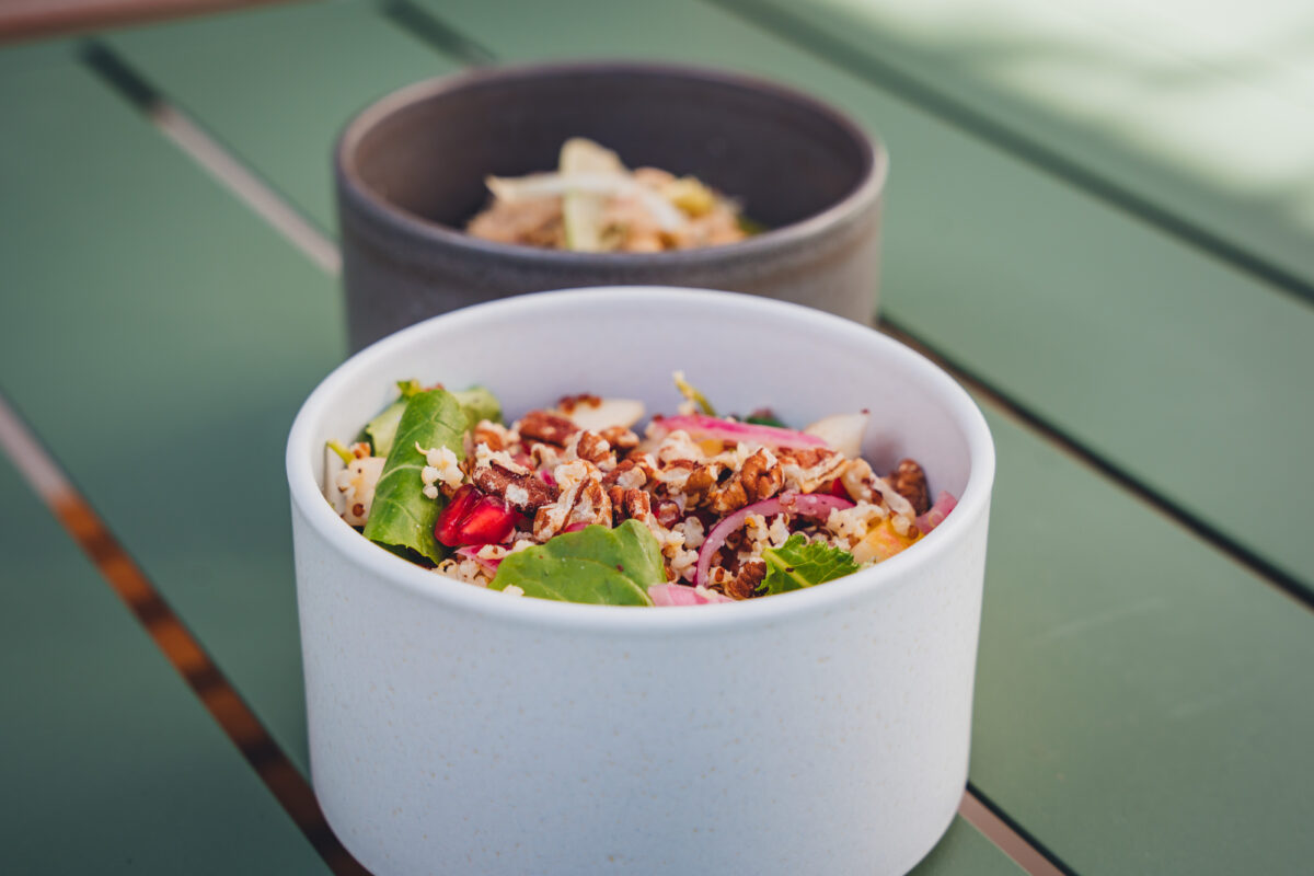 Two tall bowls. An opaque gray one smaller than a bright white one. Delicious salads inside.