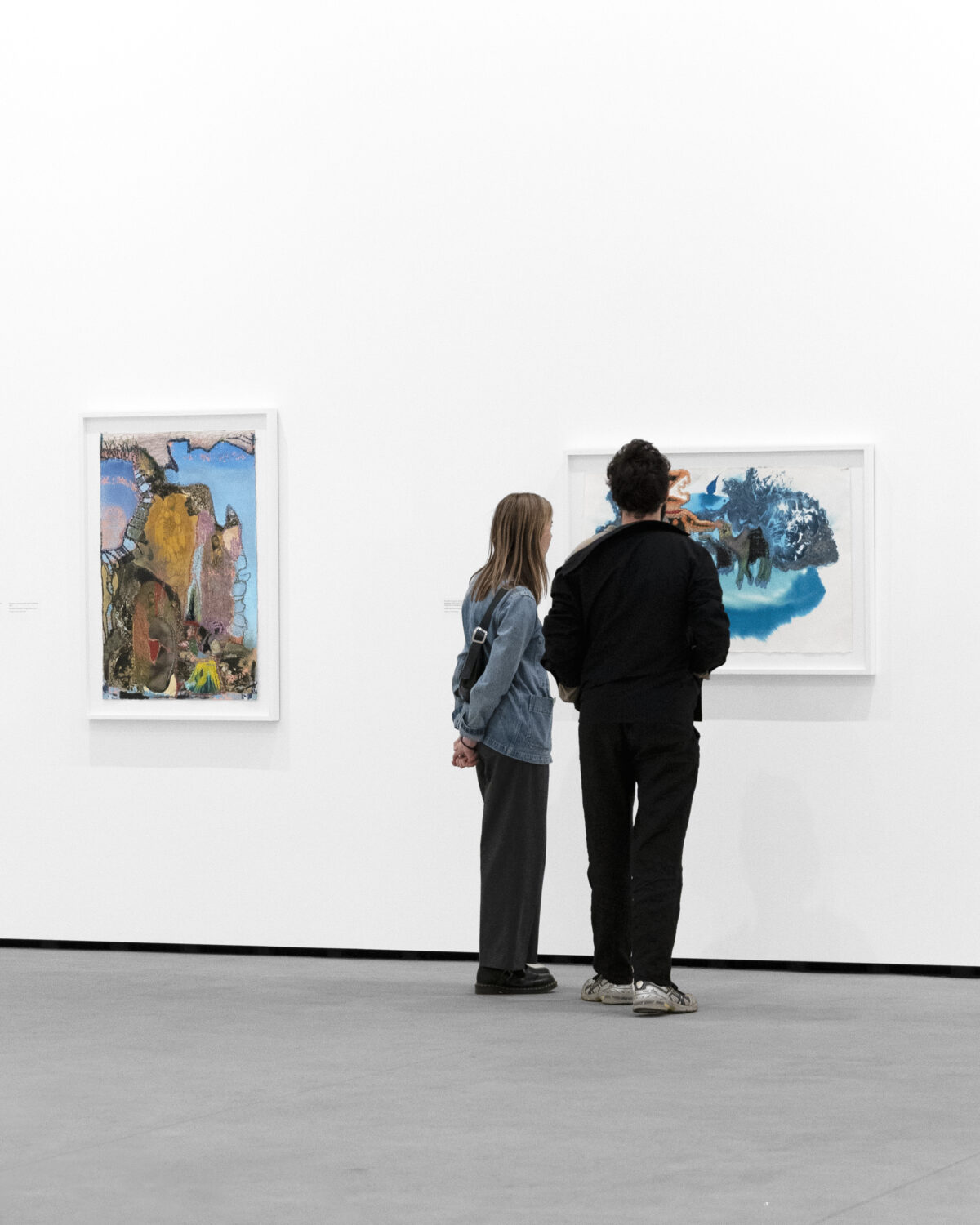 Image of two people wearing comfortable clothes in front of artwork in a large gallery