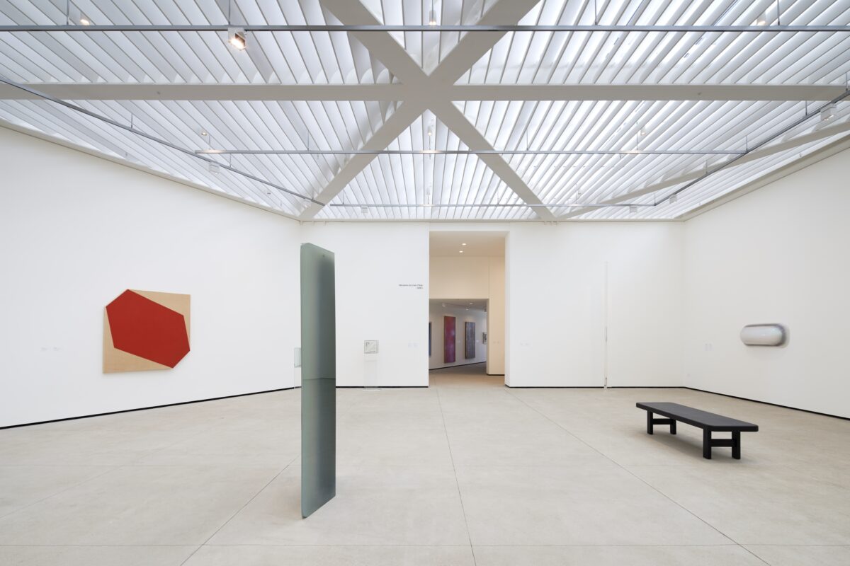 White gallery space with patterned skylight, light and space artworks on the wall and floor.