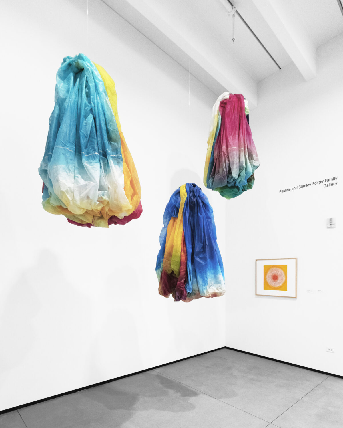 Suspended from the ceiling, three colorful canvases draped like dresses.