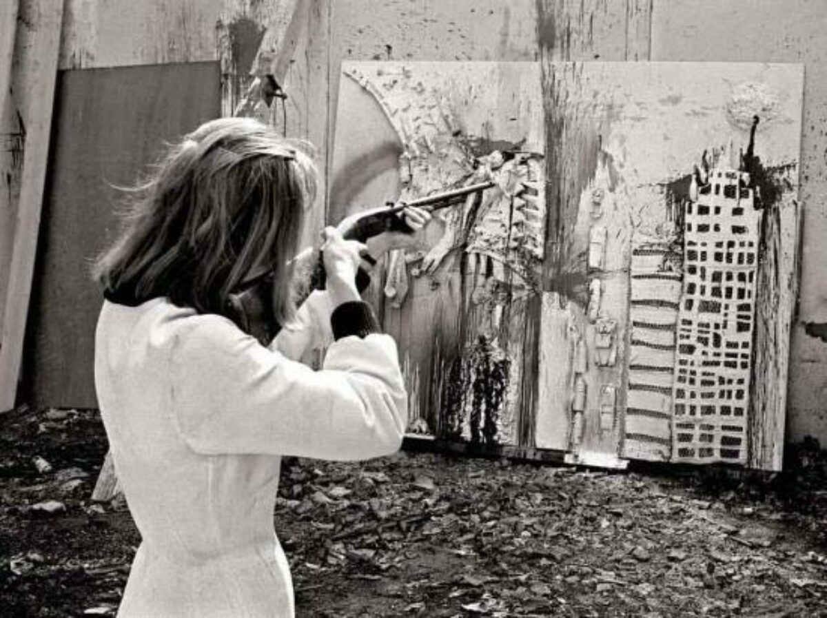 Niki Saint Phalle aiming a .22 caliber rifle. at her painting