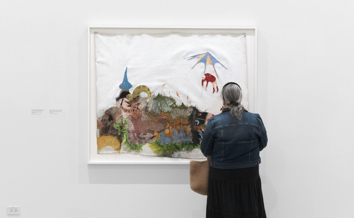 An older adult looks at an embroidered artwork of a horse.