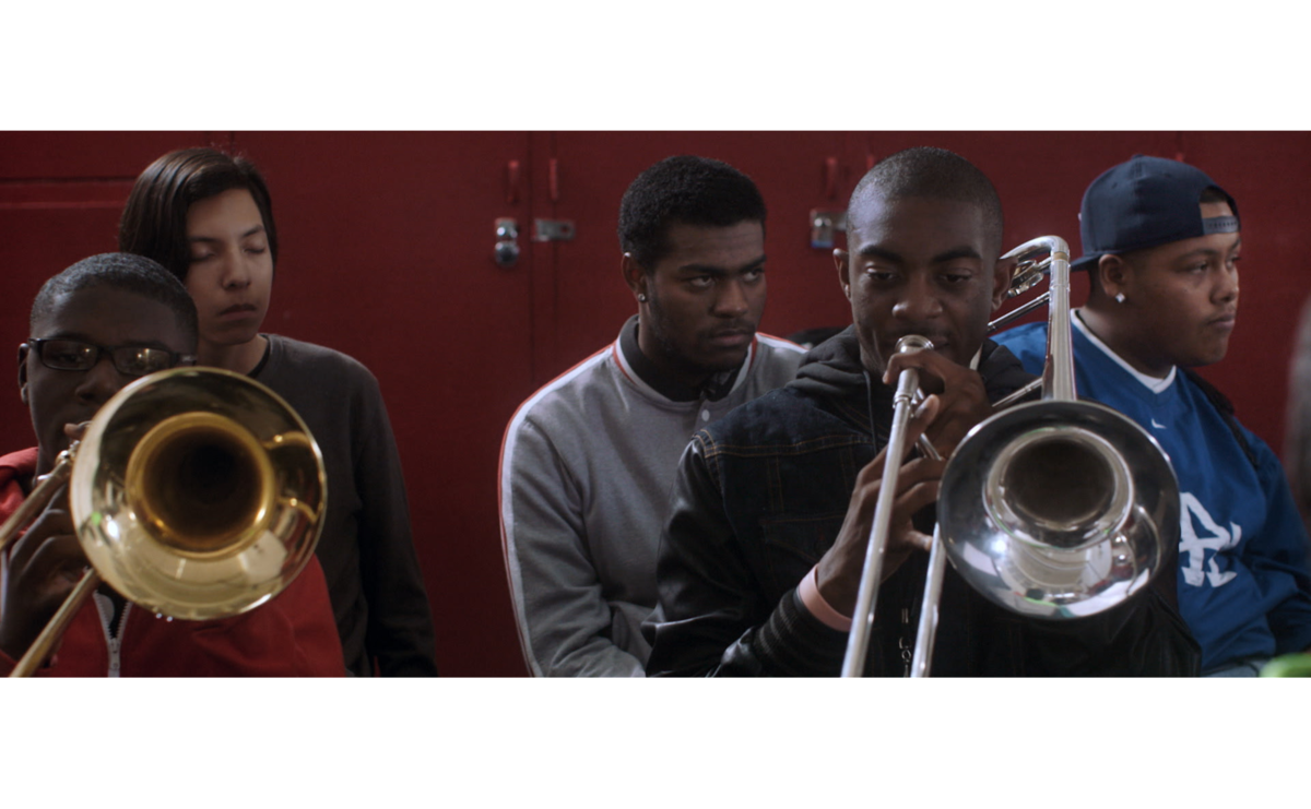 Two people playing trombones. Two people listen.