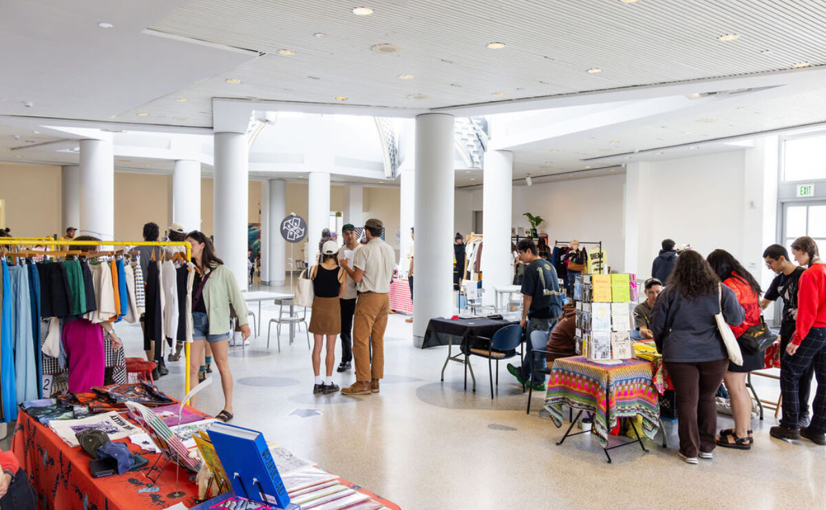 Clothing and book vendor tables in a large event space. People look at the wares.