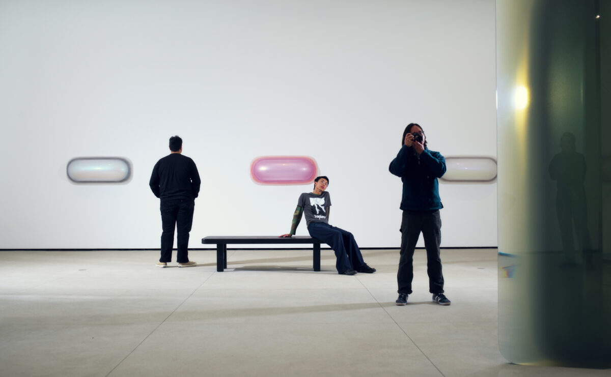 Three people in a gallery contemplating light-based artworks