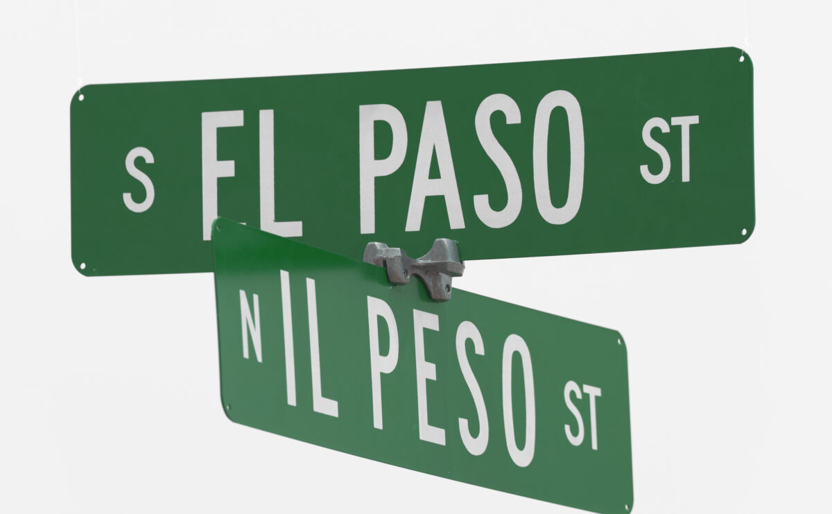 Green crossed street signs read the correct Spanish "Il Peso" and the English interpretation "El Paso" against a stark white background