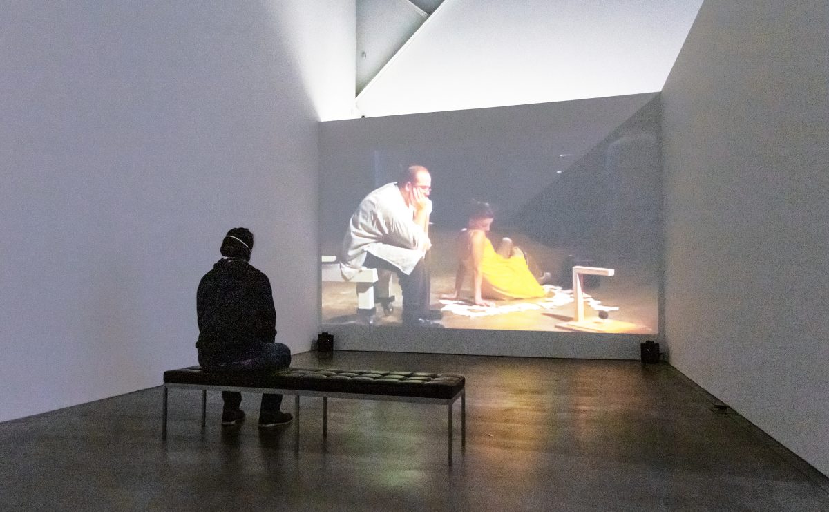 A person on a black bench with headphones on watching a projection in a dim room