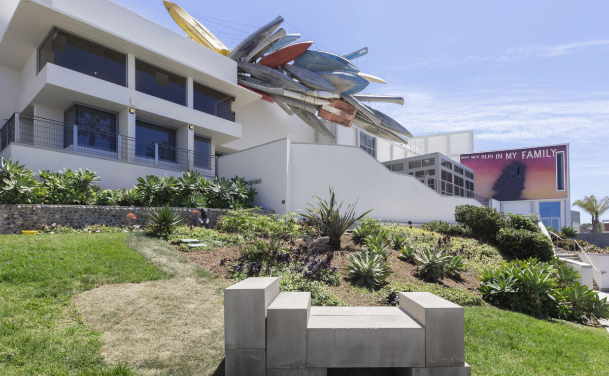 A fleet of kayaks hangs suspended from the roof of a white building, as if ready to embark on a new adventure.