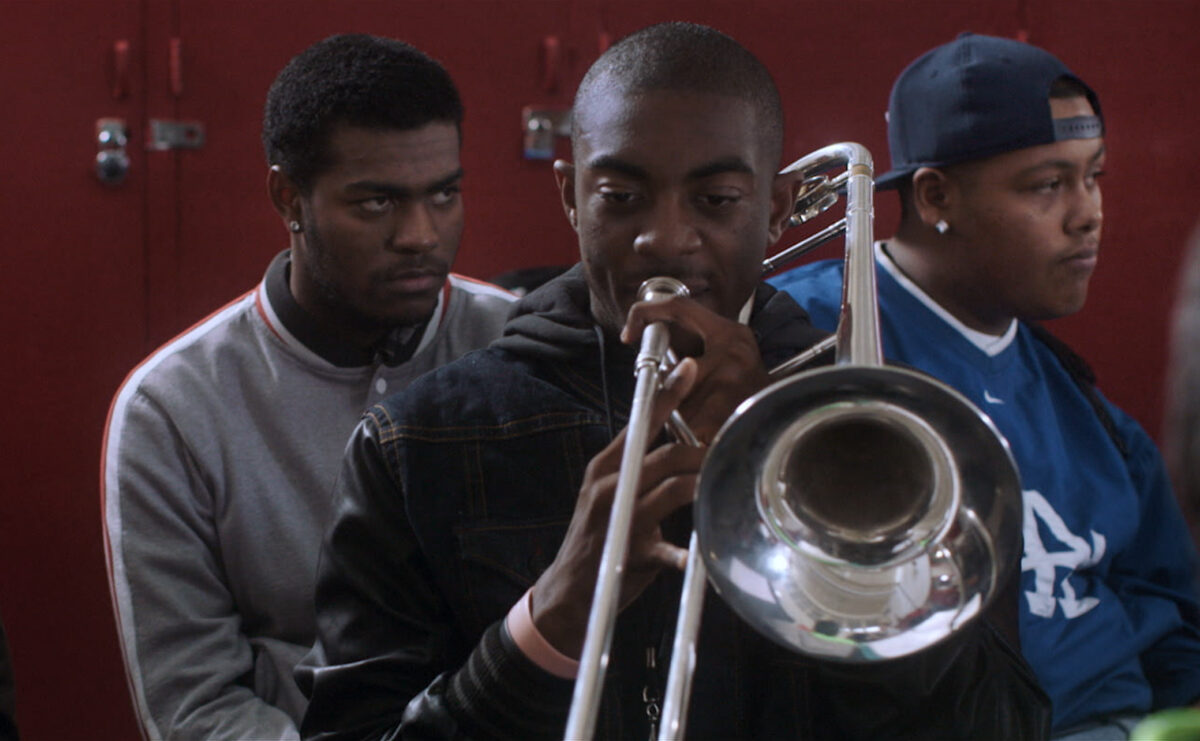 Two high school students play the trombone. Three students listen.