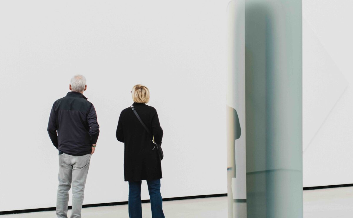 Two older adults in a gallery. To their right is a light and space artwork.