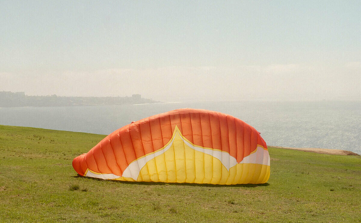 Warm colored parachute sits on a grassy hillside with an ocean view in the background