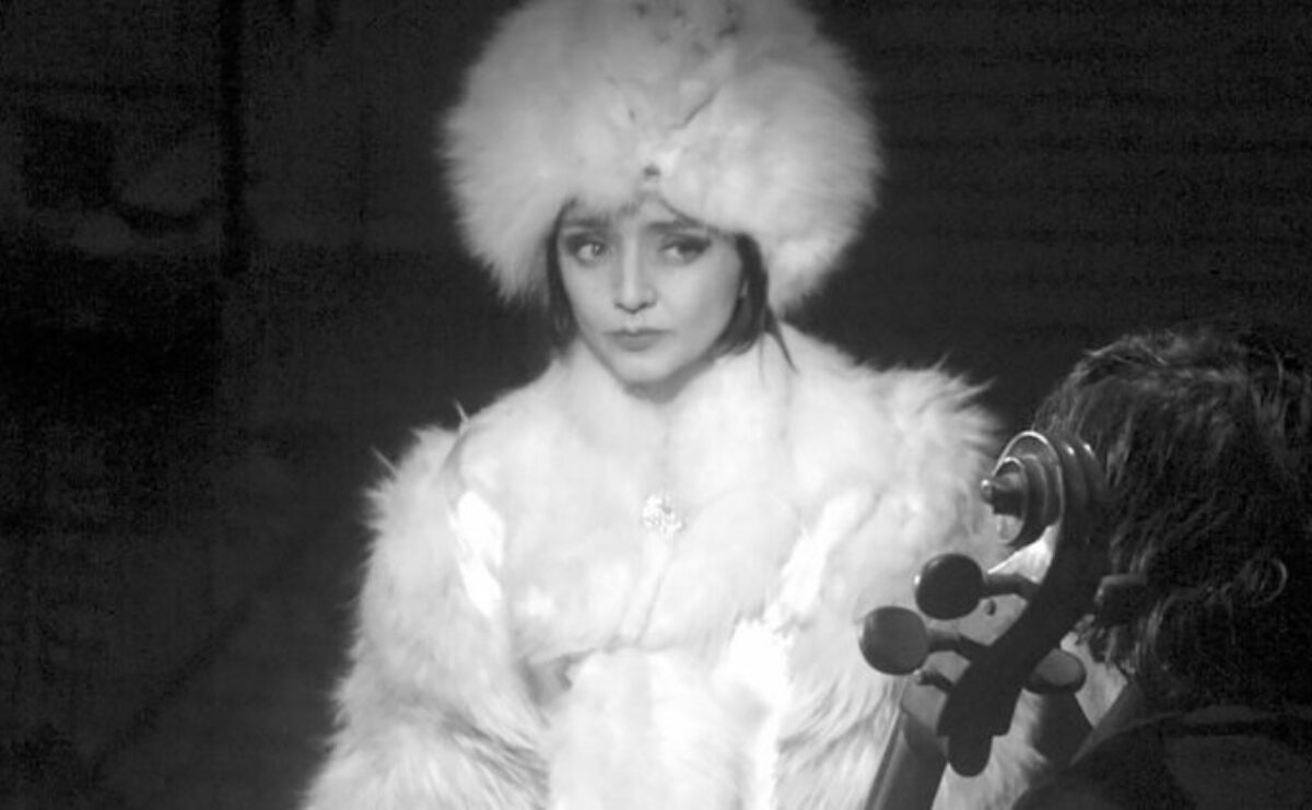 black and white image of woman in all white fur, a string instrument is in view in the foreground