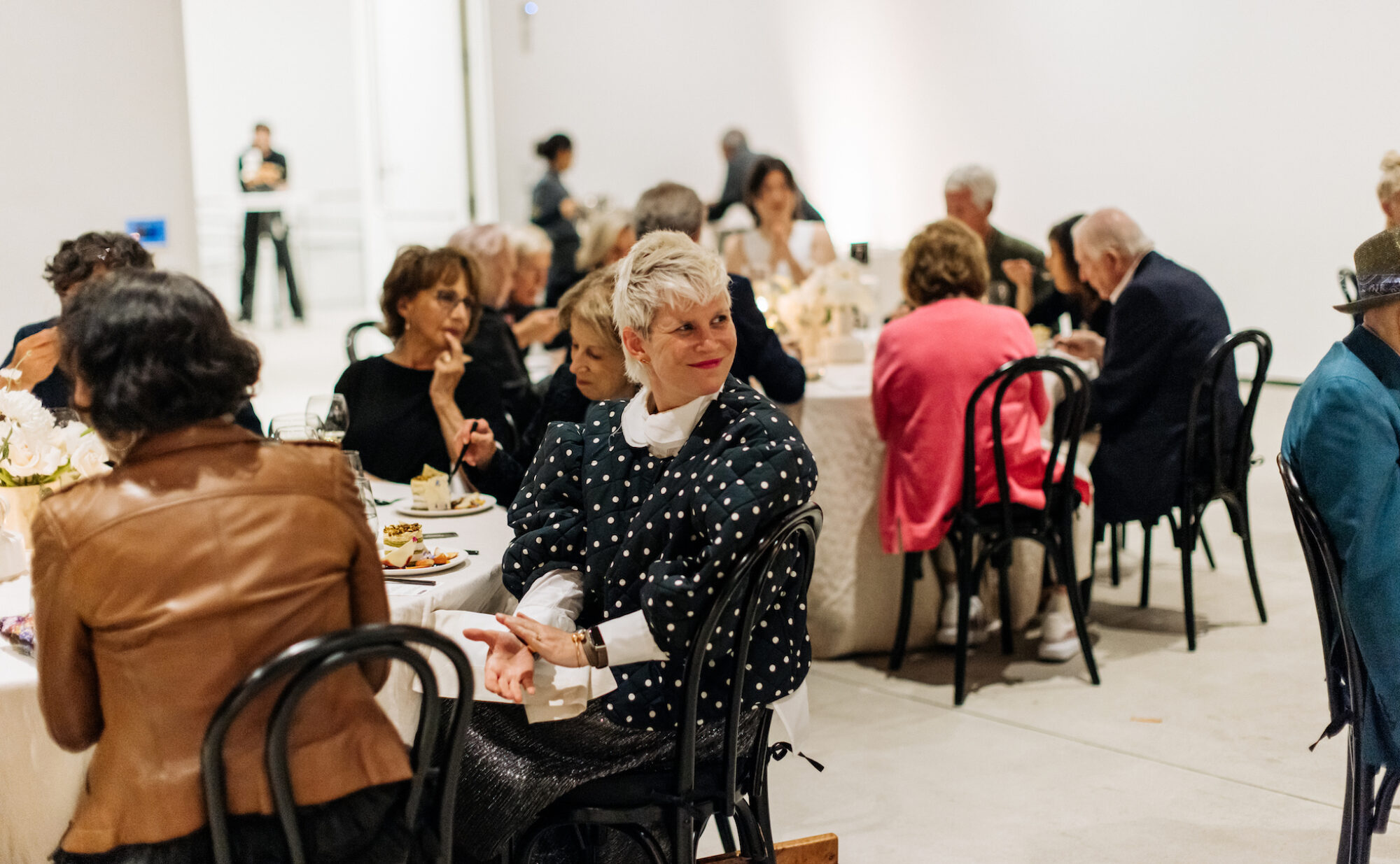 Person wearing polka-dotted outfit smiling and clapping sitting down at dinner table