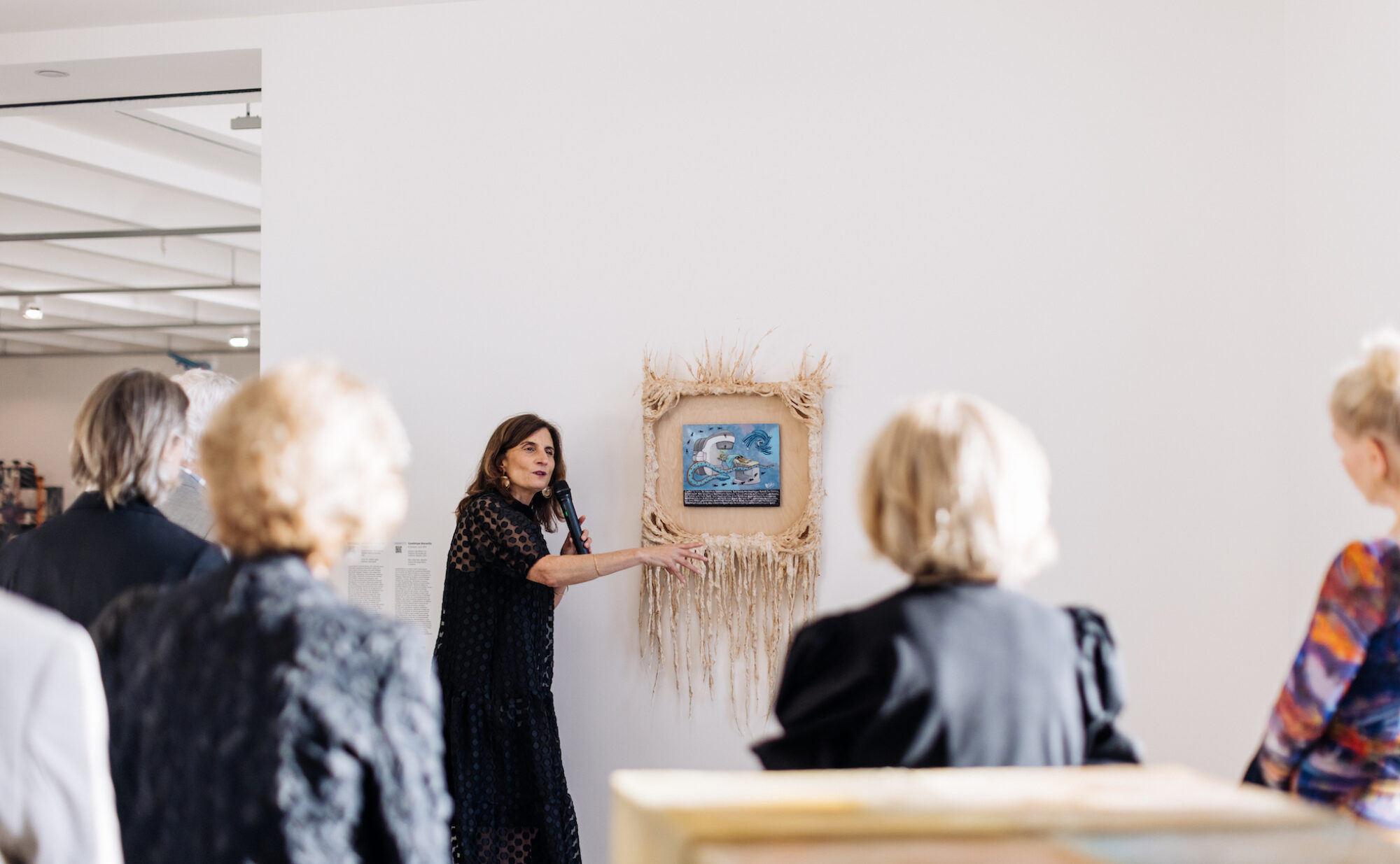 Photo of curator standing in front of artwork talking about the piece with about four people shown around her listening