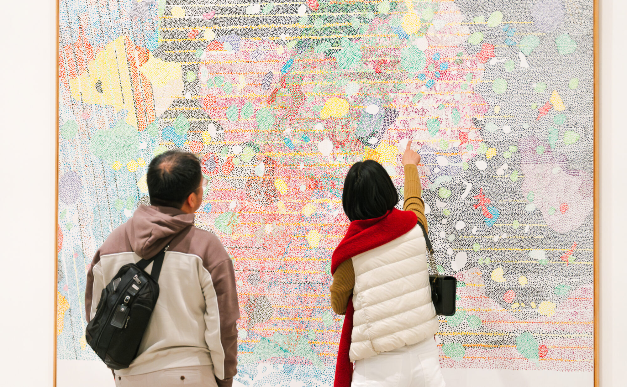 Two people looking at a large colorful canvas. One person points upwards to it.