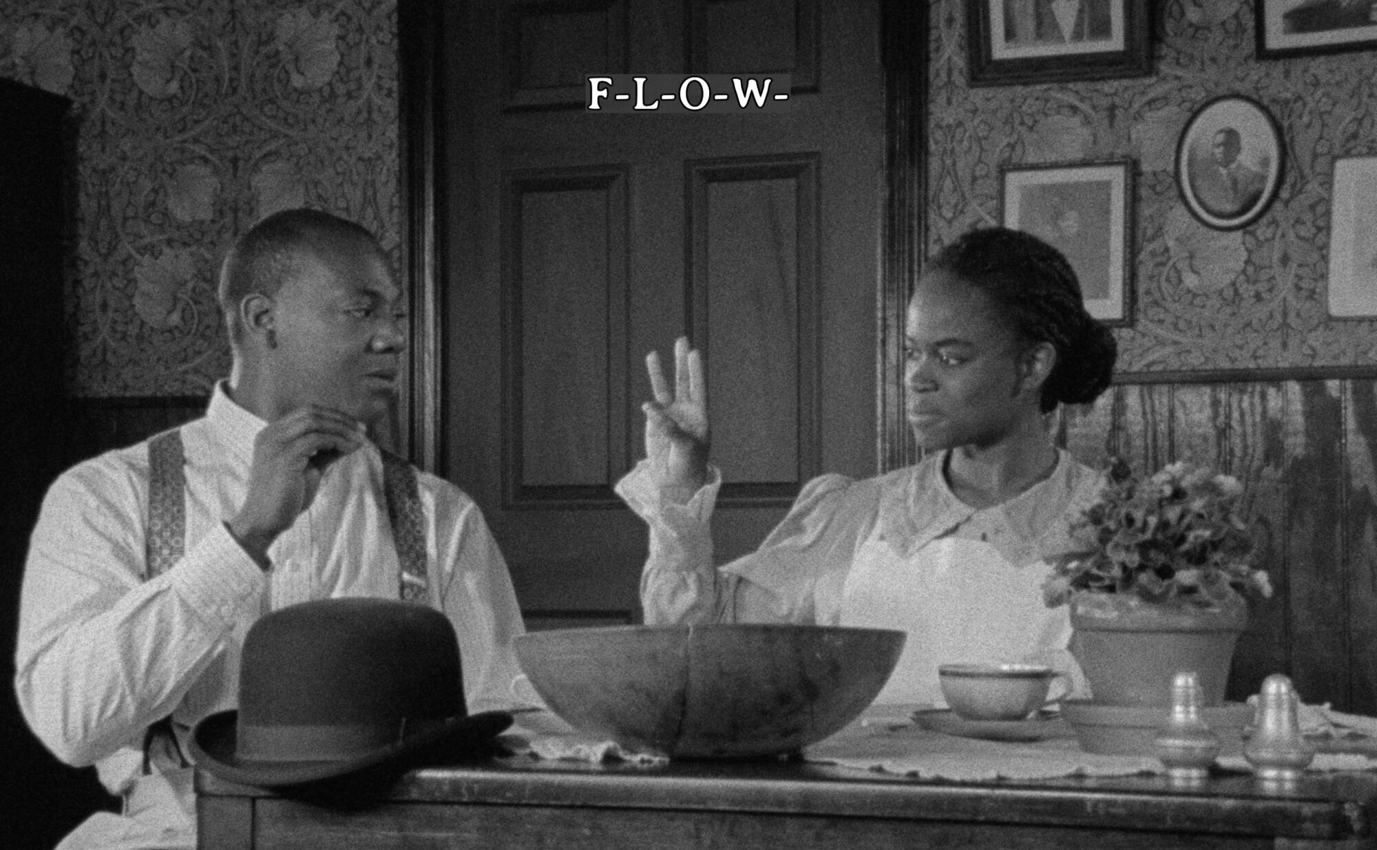 black and white film still of two black people sitting at a dinner table. one signs in ASL to the other.