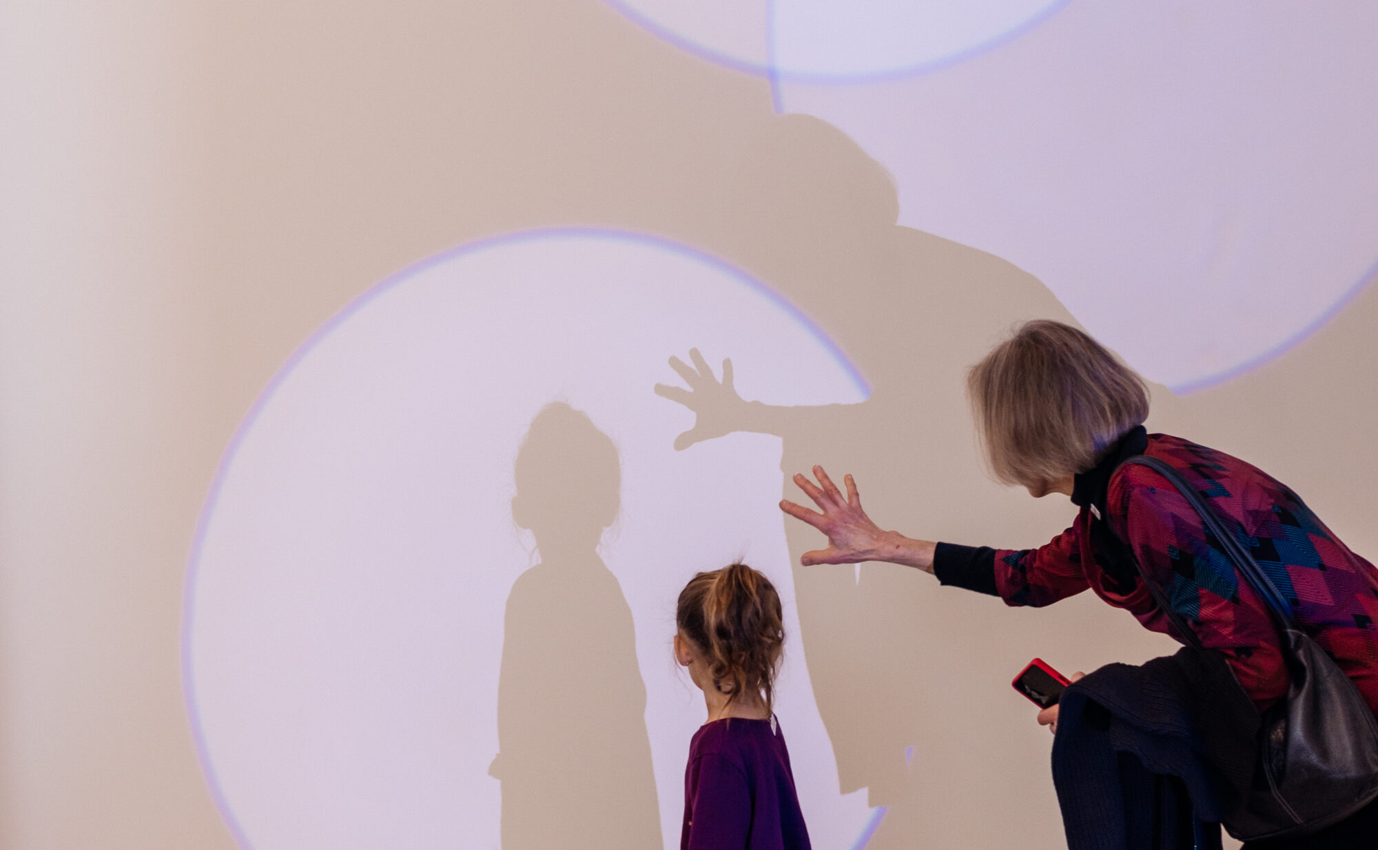 a child and guardian with their backs turned to the wall, which is illuminated with various spotlights