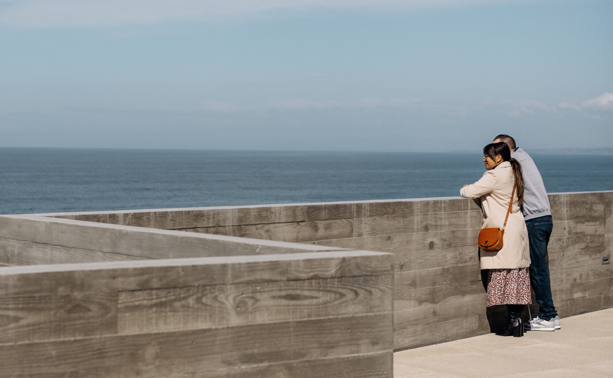 Two people stand on a terrace overlooking the ocean.