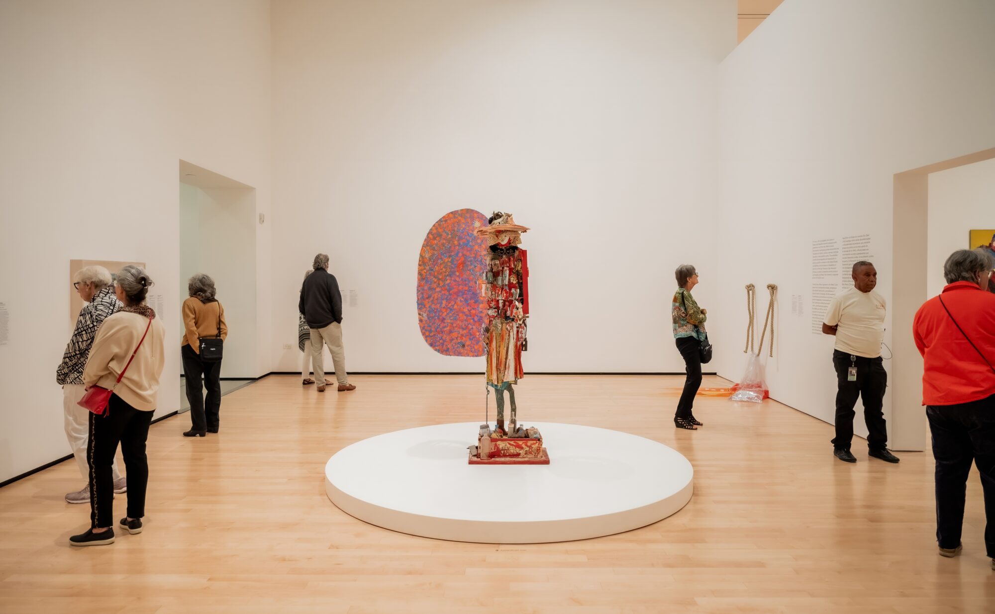 People in a gallery looking at art. At the center is an upright installation made of found objects.