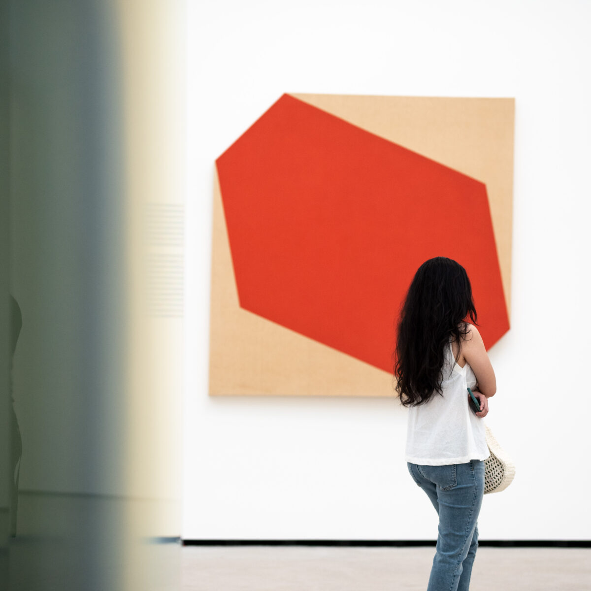 Person with long hair standing in front of abstract piece Little Blank Riding Hood by Larry Bell
