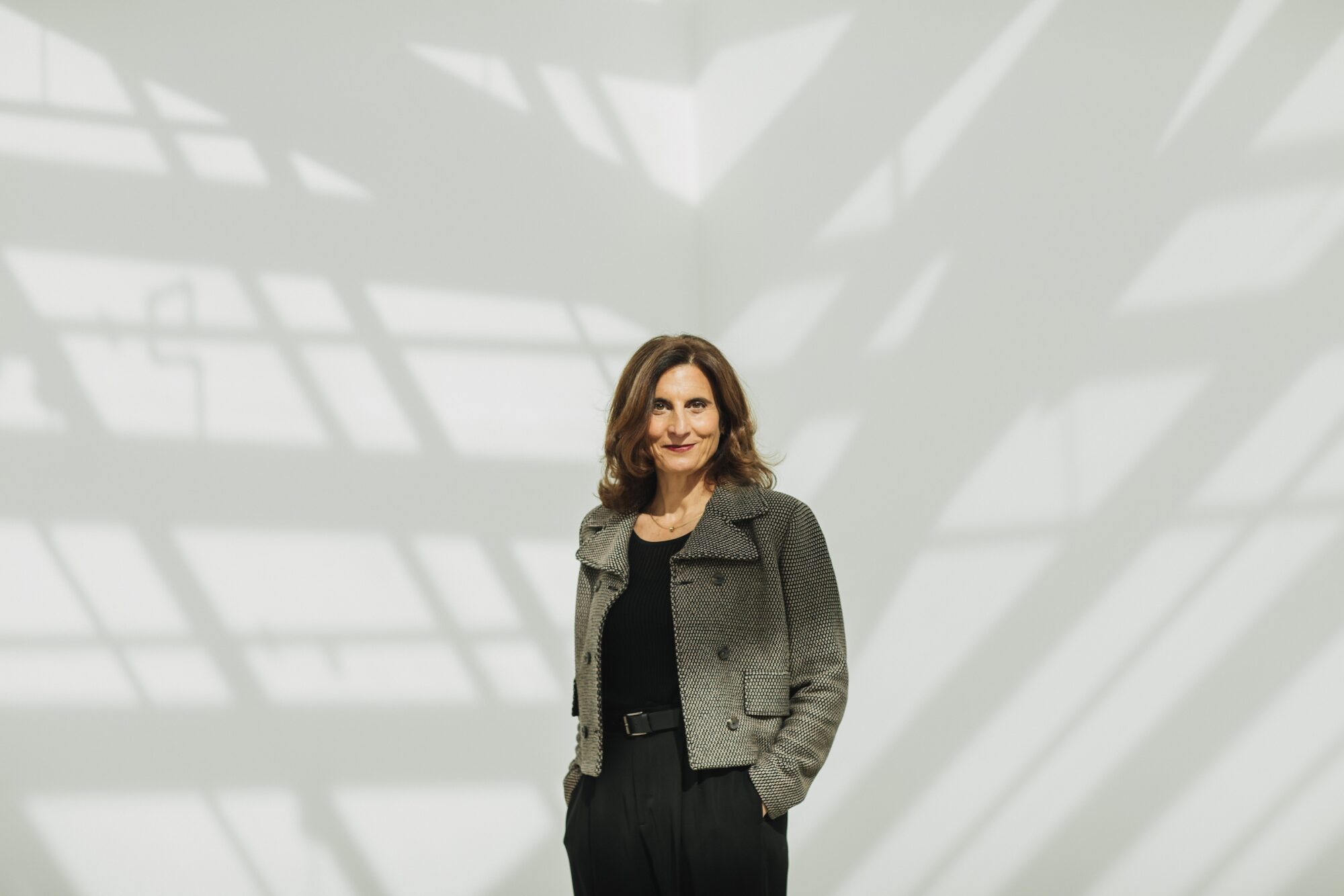 Kathryn Kanjo portrait in front of white wall, and strong shadows.