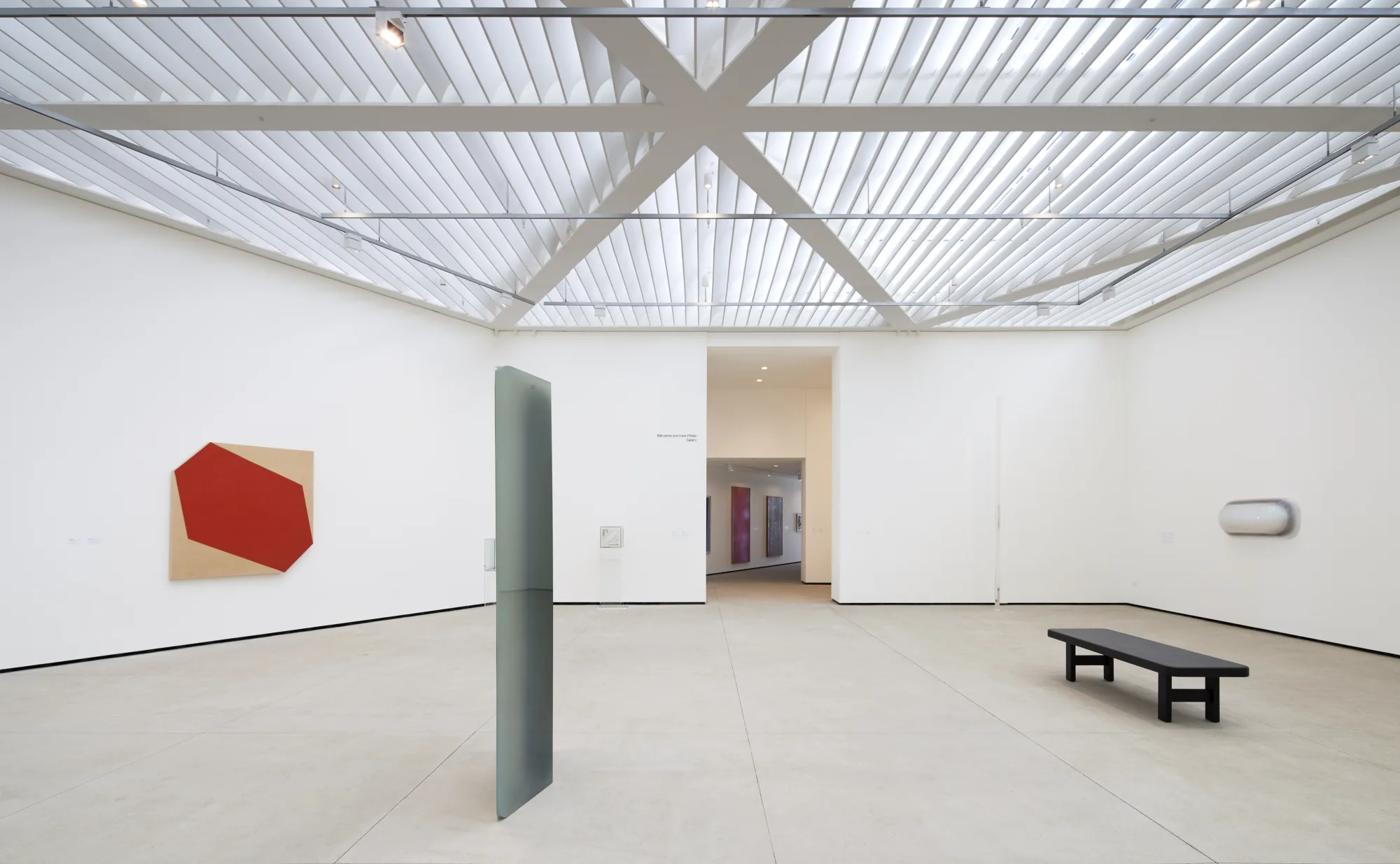 White gallery space with patterned skylight, light and space artworks on the wall and floor.